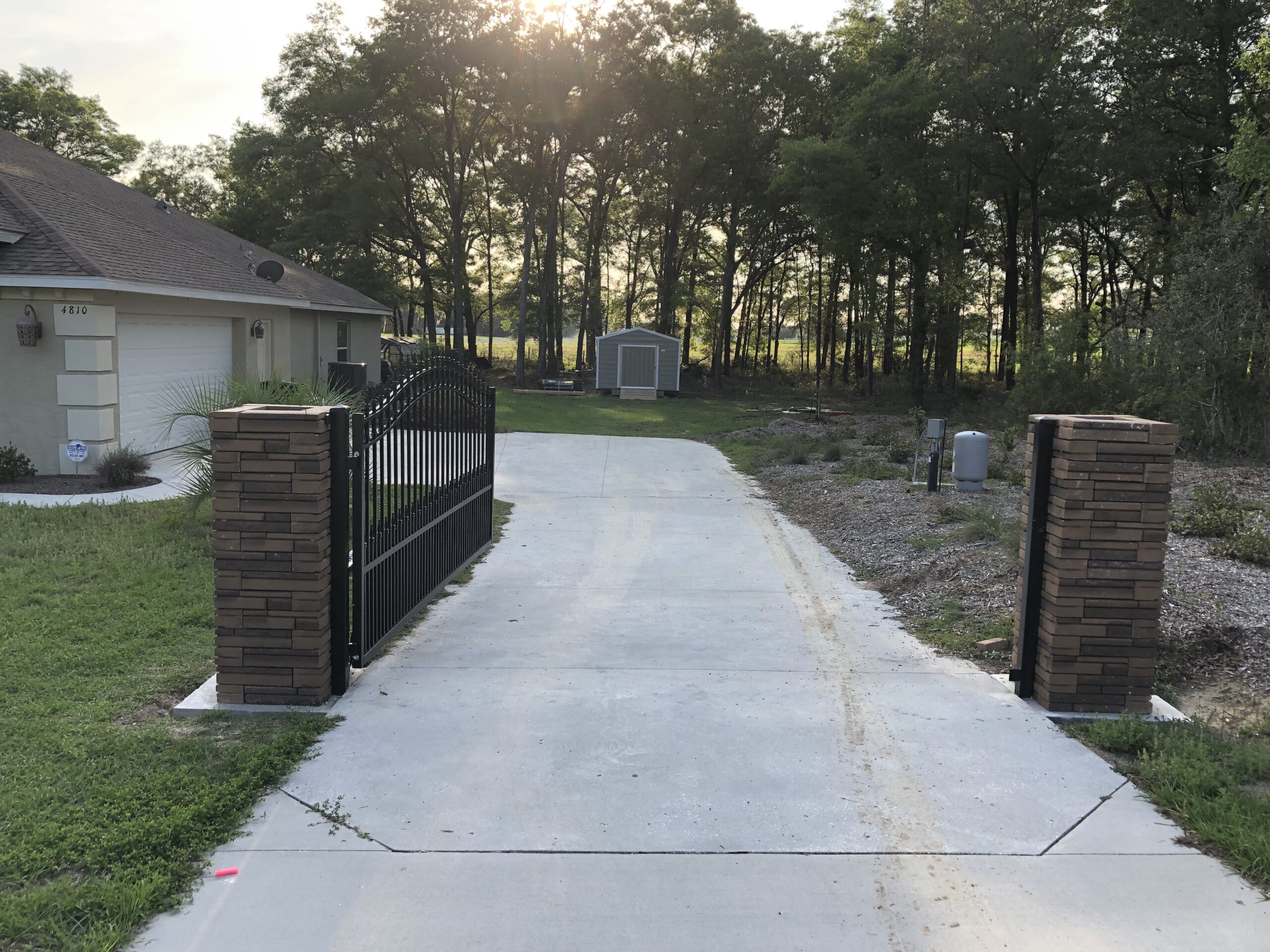 Black aluminum driveway gate between brick pillars